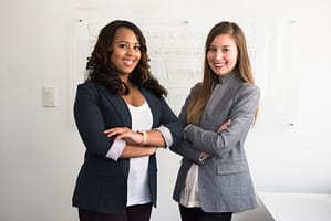 Two young women wearing business attire and smiling